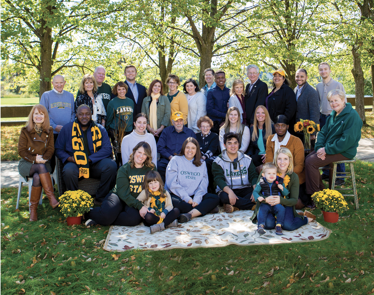 Pictured: Alumni and future and current students of SUNY Oswego posing for photo on grass outside of Tyler Hall at SUNY Oswego