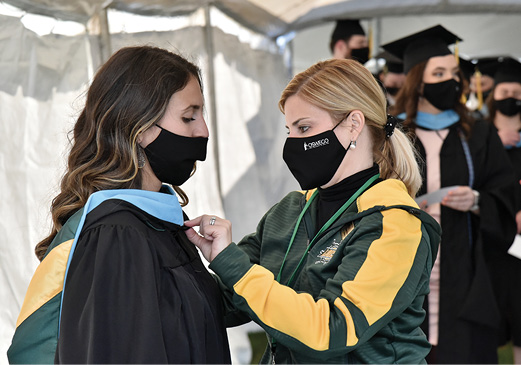 Kristen Eichorn assists a graduate with gown
