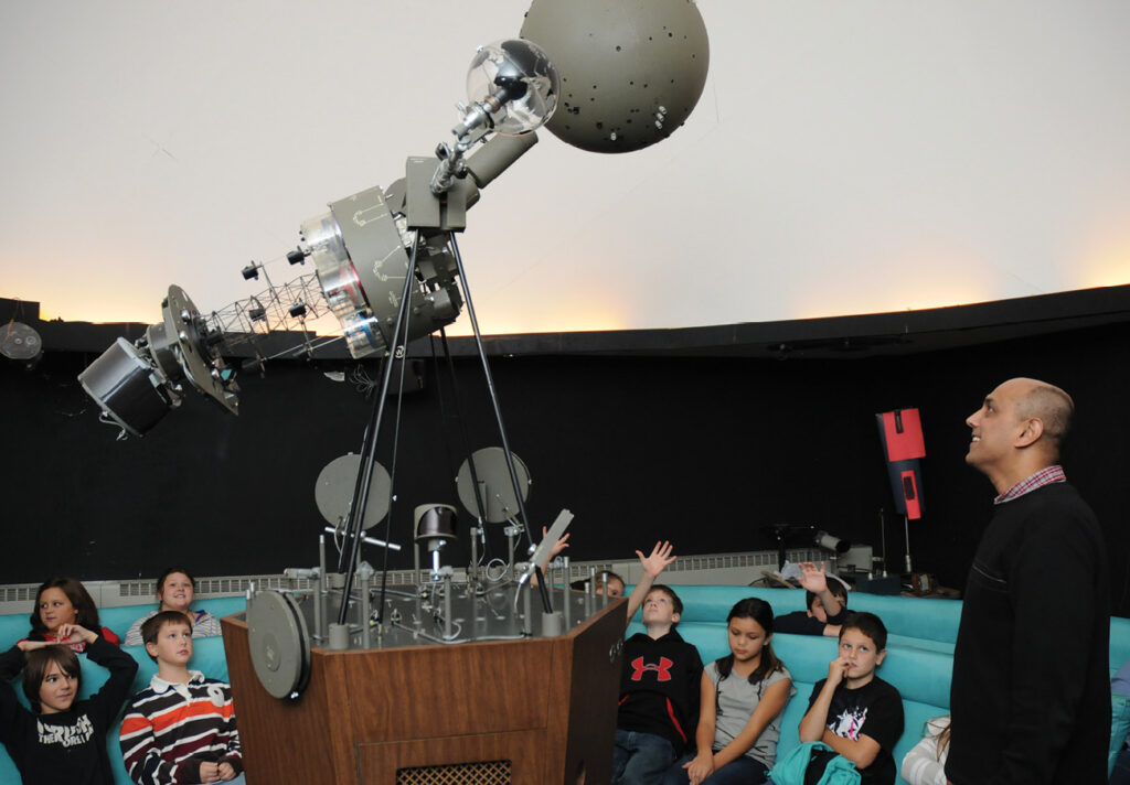 Physics Professor Shashi Kanbur talks with a visiting 5th grade class from Oswego’s Leighton Elementary School in the Piez Hall planetarium in October 2009.