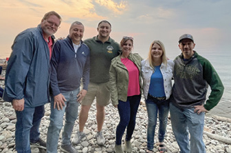 Members of the OAA board and friends gather along the lakeshore to catch the sunset during Reunion Weekend 2023. 