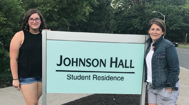 Kaleigh '22 and Sarah '97 in front of the Johnson Hall Student Residence sign at SUNY Oswego